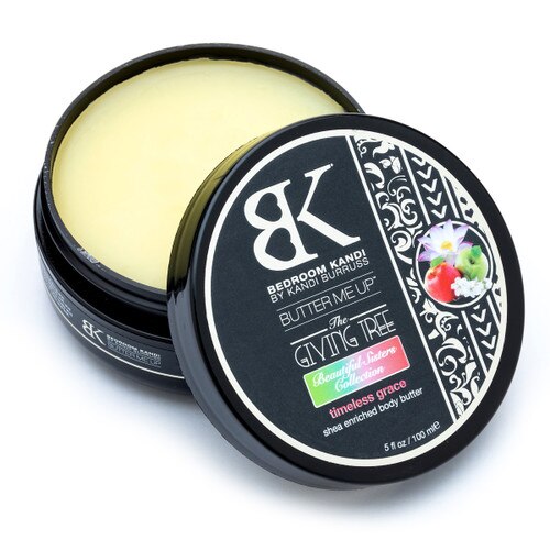 An image of a round container of Butter Me Up in the Timeless Grace scent. The container is open with the lid propped up in front of it, revealing the smooth pale yellow surface of the body butter.